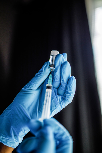 Close up shot of unrecognizable nurse, wearing disposable gloves, drawing a vaccine or a shot in a syringe from a vial.