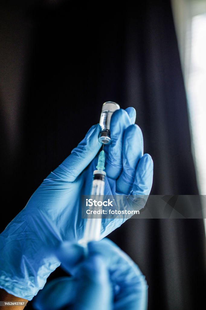 Nurse wearing disposable gloves, holding a syringe with vaccine or a shot Close up shot of unrecognizable nurse, wearing disposable gloves, drawing a vaccine or a shot in a syringe from a vial. Vaccination Stock Photo