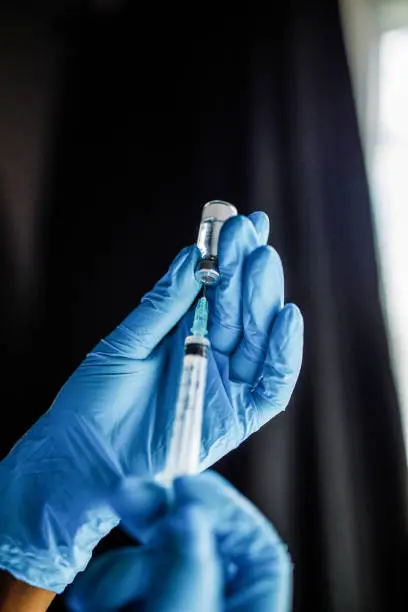 Close up shot of unrecognizable nurse, wearing disposable gloves, drawing a vaccine or a shot in a syringe from a vial.