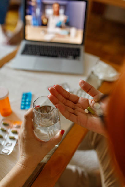 mujer sosteniendo píldoras y cápsulas en la palma de su mano, a punto de tomarlas con un vaso de agua - antibiotic red medicine healthcare and medicine fotografías e imágenes de stock