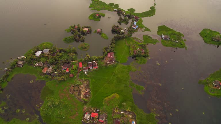 Drone flying forwards revealing several humble houses on lawns surrounded by water after flooding