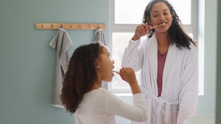 Family home, bathroom and brushing teeth with mother and daughter learning good hygiene and dental habits for health and wellness. Black woman and girl child cleaning mouth together in morning