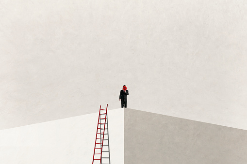 A man, having climbed a ladder to reach the top, shouts through a large red megaphone.