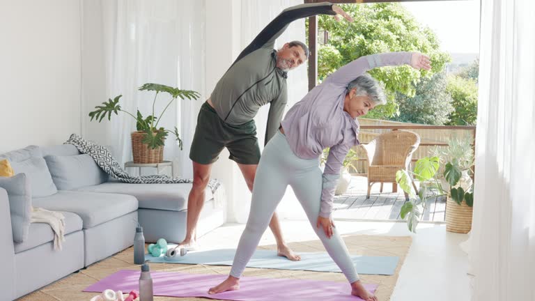 Fitness, exercise and senior couple in home doing workout, yoga and pilates in living room together. Wellness, health and elderly man and woman exercising, stretching and cardio training on yoga mat