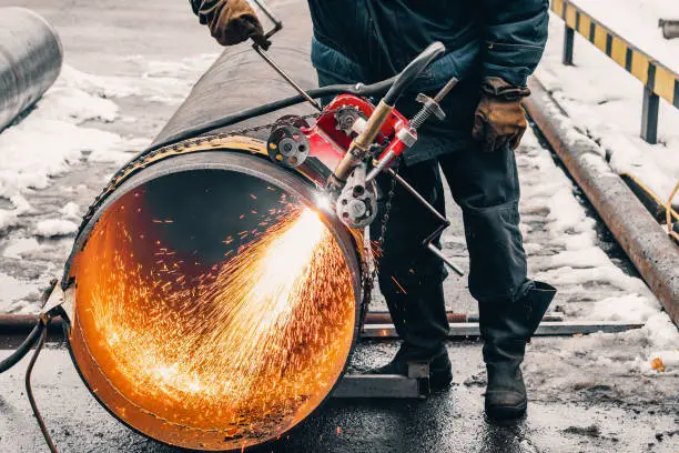 Working welder cuts metal and sparks fly. Gas cutting of large diameter pipes with acetylene and oxygen. Industrial metal cutting in oil and gas industry.