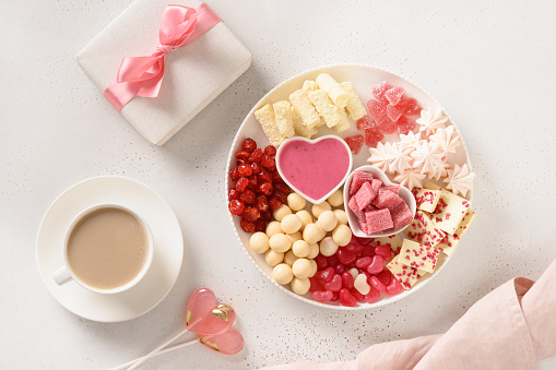 Romantic coffee for two, gift, heart shaped lollypop and Valentine's Day charcuterie board with chocolate sweets and strawberries on white background. Copy space.