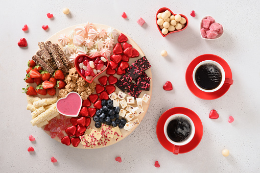 Coffee for two and Valentine's Day charcuterie board with red chocolate sweets, marshmallow and strawberries on white background. Sweet romantic appetizer.