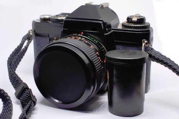 istock old analog camera in black color, connected on its synthetic material strap, with a plastic 35 mm film package beside it, on a white background. 1452704976