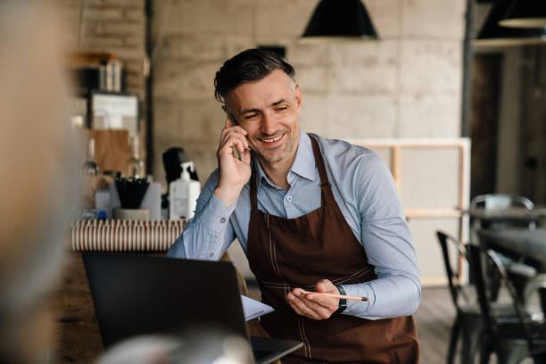 istock Adult white waiter using cellphone and laptop while working in cafe 1452706529
