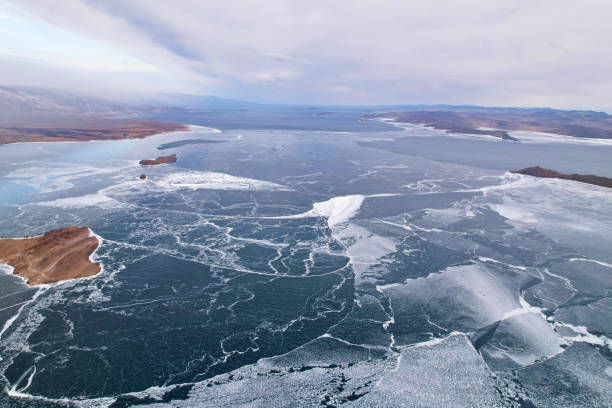 lago ghiacciato baikal a dicembre, vista aerea. cielo tempestoso nuvoloso, ghiaccio trasparente nelle fessure. - lake baikal lake landscape winter foto e immagini stock