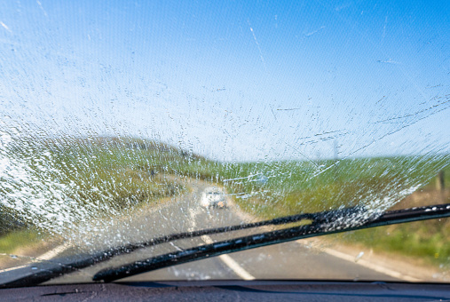A windscreen wiper moving up to clear the windscreen wash fluid sprayed, as a car approaches on an English country road.