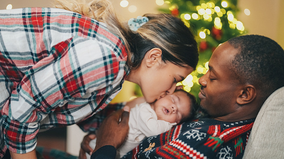 Mixed race family with newborn baby enjoying cozy Christmas evening at home
