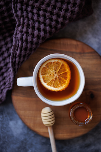 Istanbul, Turkey-December 27, 2022: Black tea with dried orange slices in a white ceramic cup on wooden presentation board. Next to the cup is a purple linen napkin, honey stick and a small jar of honey. Shot with Canon EOS R5.