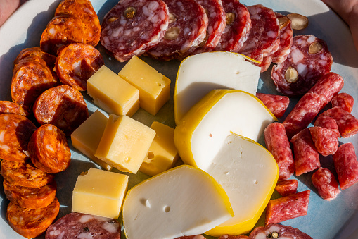 Cured meat and cheese platter. Charcuterie board filled with mixed spanish chorizo slices, various salami pieces and cheeses. Natural sun light. High angle view. Food background with copy space.