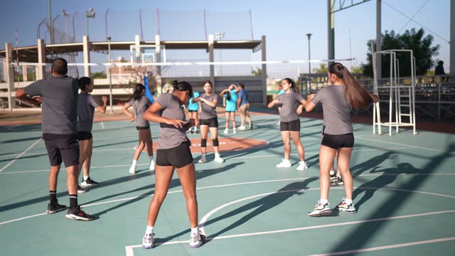 Female team stretching during warm-up with their coach at sport court
