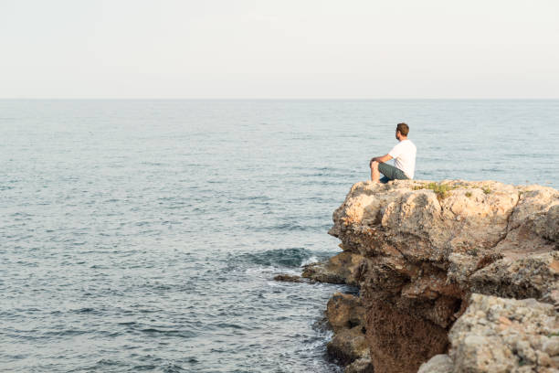 istock Man sitting on a mediterranean cliff at sunset. 1452719737