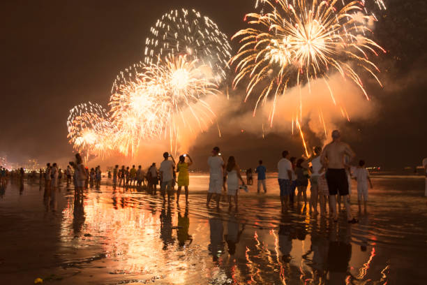 silvesterfeier am strand. menschen, die das feuerwerk am wasser beobachten. - dark edge stock-fotos und bilder