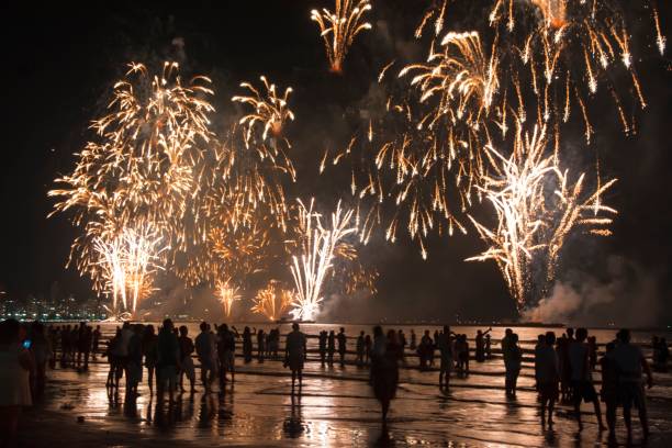 celebração de ano novo na praia. pessoas assistindo aos fogos de artifício à beira da água. - dark edge - fotografias e filmes do acervo