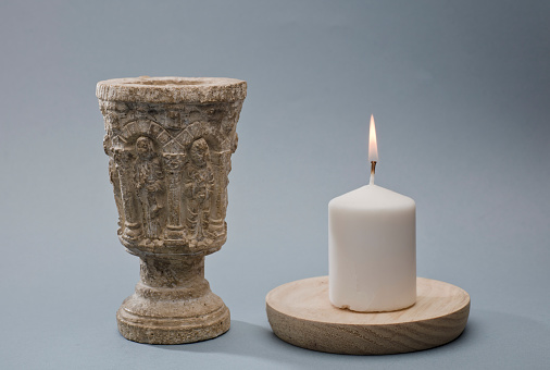 stone chalice with white candle light blue background, space for text
