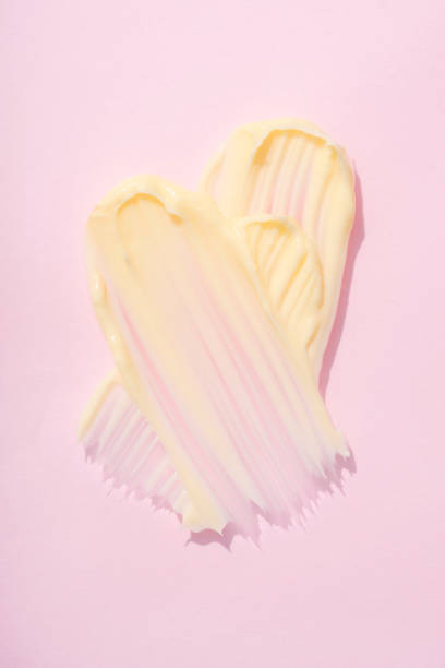 вертикальное изображение шелковистой текстуры косметического крема. крем или масло для тела размазывается по розовому фону. средство по у� - shea butter moisturizer butter cream стоковые фото и изображения