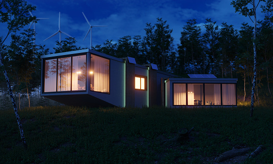 Modern designed energy efficient house with solar panels and wind turbines behind it, night scene. (3d render)