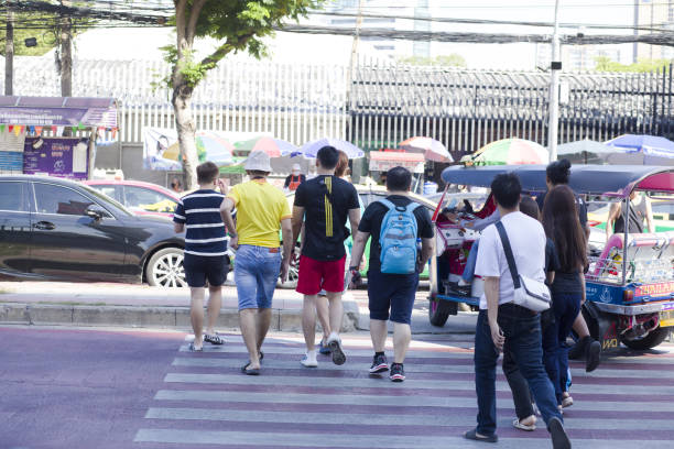 Walking  tourists on zebra crossing in Bangkok are crossing street Kampheng Phet Road. People are on way to Chatuchak Weekend market in Bangkok, where is one of main entrance gates