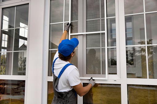 Installation of a mosquito net on a large window outside a modern building. An experienced installer installs a protective net against insects on a plastic window