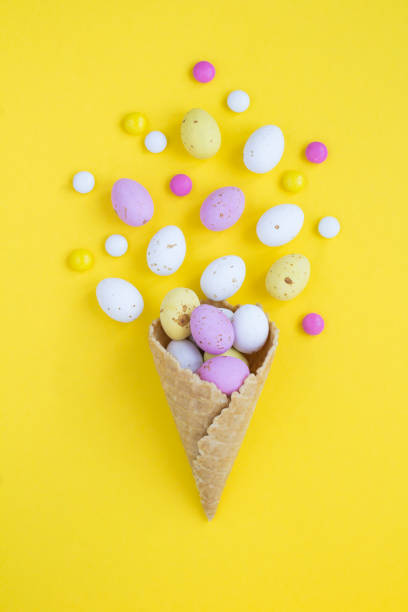 istock Ice cream cone with colored easter eggs on the yellow background. Top view. Close-up. 1452735045