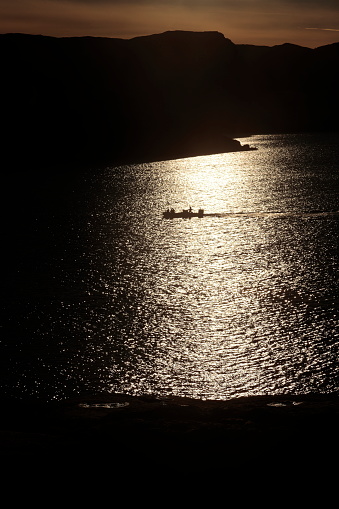 Ein kleines Motorboot fährt in der Abendsonne durch den Lichtschein, das Foto ist stark unterbelichtet.