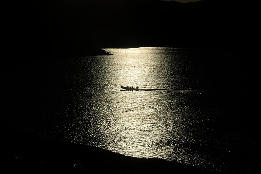 A small motorboat drives through the light in the evening sun, the photo is severely underexposed.
