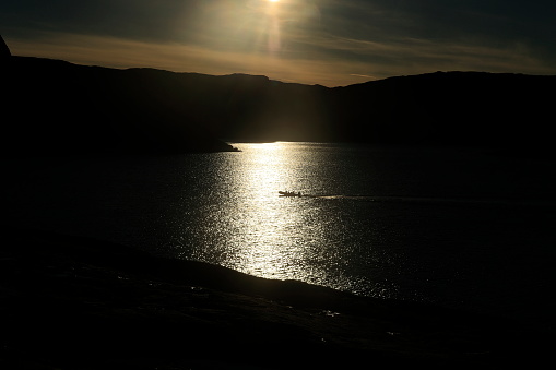 Ein kleines Motorboot fährt in der Abendsonne durch den Lichtschein, das Foto ist stark unterbelichtet.