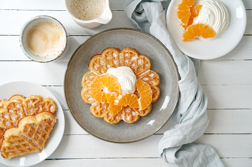 Waffles, tangerines and curd cheese with a cup of coffee on a wooden table