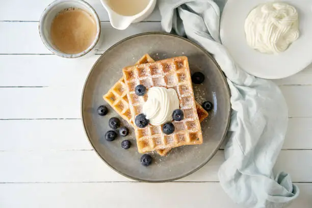 Waffles, berries and curd cheese with a cup of coffee on a wooden table
