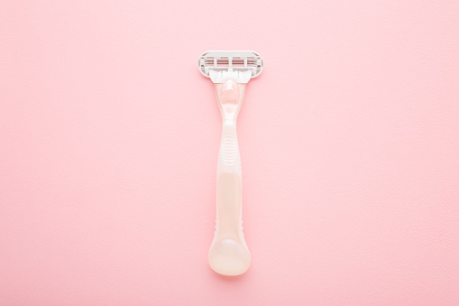 New razor on light pink table background. Pastel color. Closeup. Female product for smooth body skin. Top down view.
