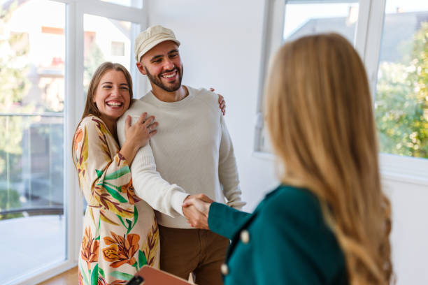 Young happy couple and an agent shaking hands in a new property stock photo