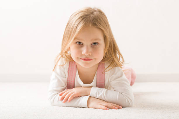 uśmiechnięta piękna dziewczynka leżąca na brzuchu na jasnobeżowym domowym dywanie. słodki 3-letni maluch. widok z przodu. zbliżenie. - carpet floor lying down people zdjęcia i obrazy z banku zdjęć