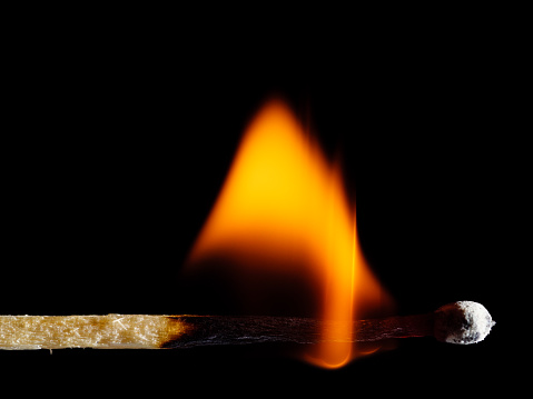 Wooden match burns with yellow fire on a black background