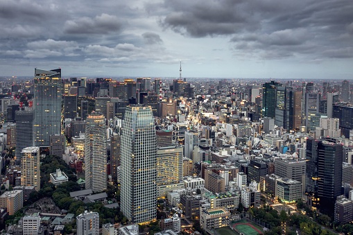 An aerial breathtaking view of a cityscape of Tokyo downtown, with modern architecture, lights turned on a cloudy evening