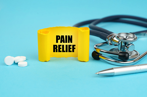 Medical concept. On a blue surface, a stethoscope, pills, a pen and a yellow sign with the inscription - PAIN RELIEF