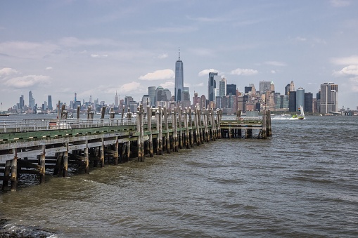 A wooden dock in the East River with a cityscape of the New York in the background, with clouds on a blue sky