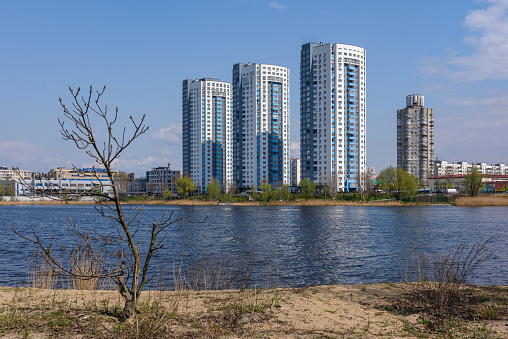 Three identical modern multi-storey houses on the shore of the lake with a dry lonely tree in the foreground. High quality photo