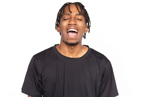 Portrait of emotional young man. Male African American model with brown eyes and afro braids in black T-shirt opening his mouth laughing, shouting with closed eyes. Emotion, facial expression concept
