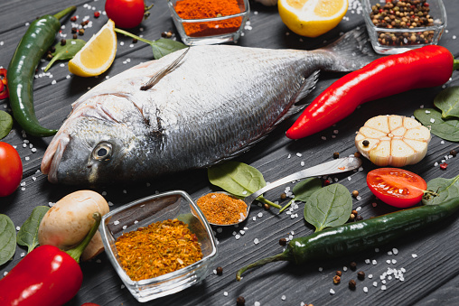 Fresh raw dorado fish on baking paper with lemon, pepper, tomatoes and various spices on wooden background with copy space.