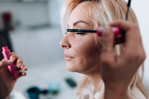 Close up makeup artist applying black mascara in pink packaging on her client's eyelashes