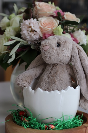A closeup shot of the Easter bunny decoration with colorful flowers behind on the table