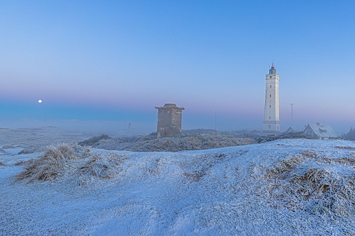 Panorama over the dunes and lighthouse of the Danish coastal resort of Blavand at sunrise on an icy winter day