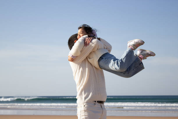 Happy father and daughter playing on beach. Japanese family walking, laughing, fooling around, lifting child up. Dad leisure, family time, parenting concept