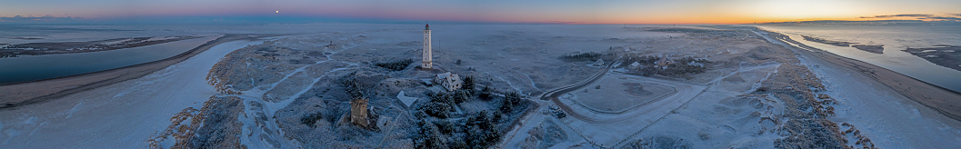 Drone panorama over the beach and lighthouse of the Danish coastal resort of Blavand at sunrise on an icy winter day