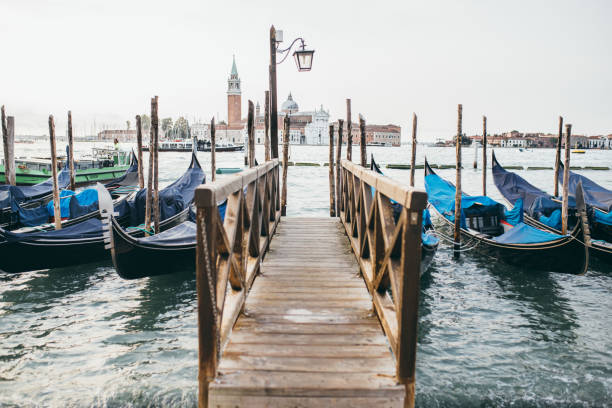 Venice, Italy - September 23, 2023: Gondola with tourists riding through the turquoise lagoon with the iconic san giorgio maggiore church and bell tower on an island in the background. Showing a vibrant cityscape under a bright blue sky