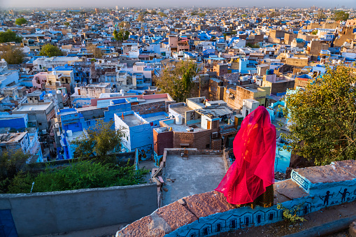 Young Indian woman looking at the view. The Blue City of Jodhpur on the background. Jodhpur is known as the Blue City due to the vivid blue-painted houses around the Mehrangarh Fort.